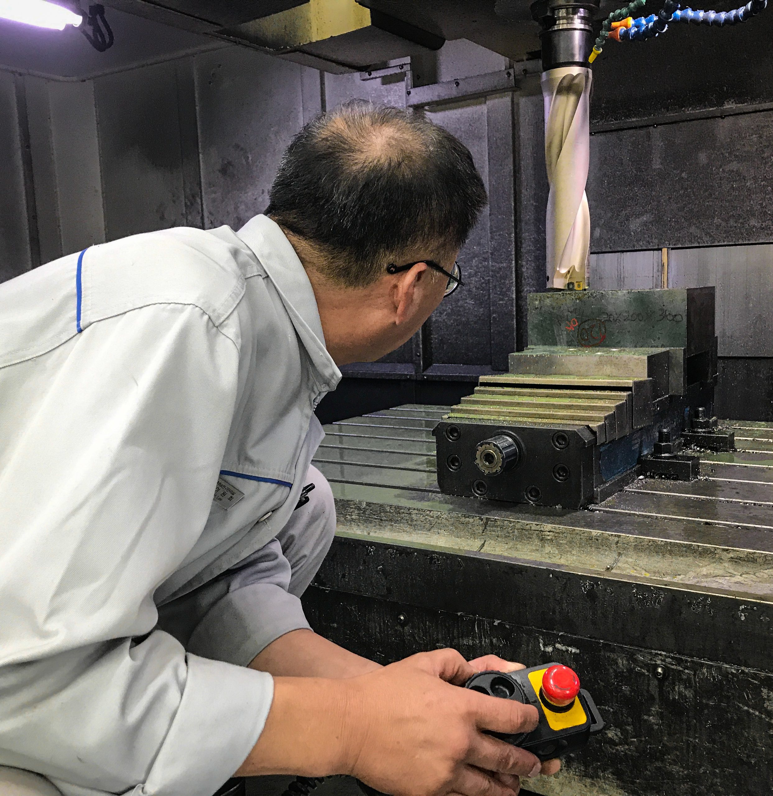 Mann hält Steuergerät und blickt auf rotierendes Fräswerkzeug der CNC‑Maschine