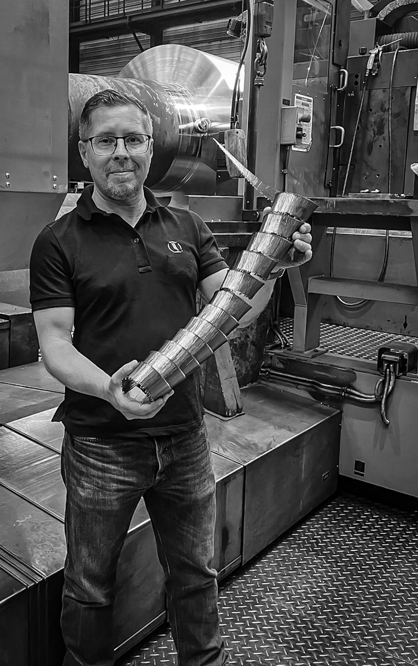 Mann hält vor einer Drehmaschine einen langen spiralförmigen Metallspan